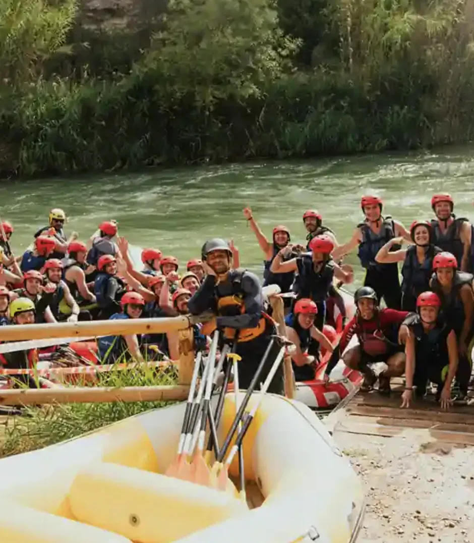 Grupo de adultos con equipamiento de rafting junto a un río antes de una actividad física al aire libre